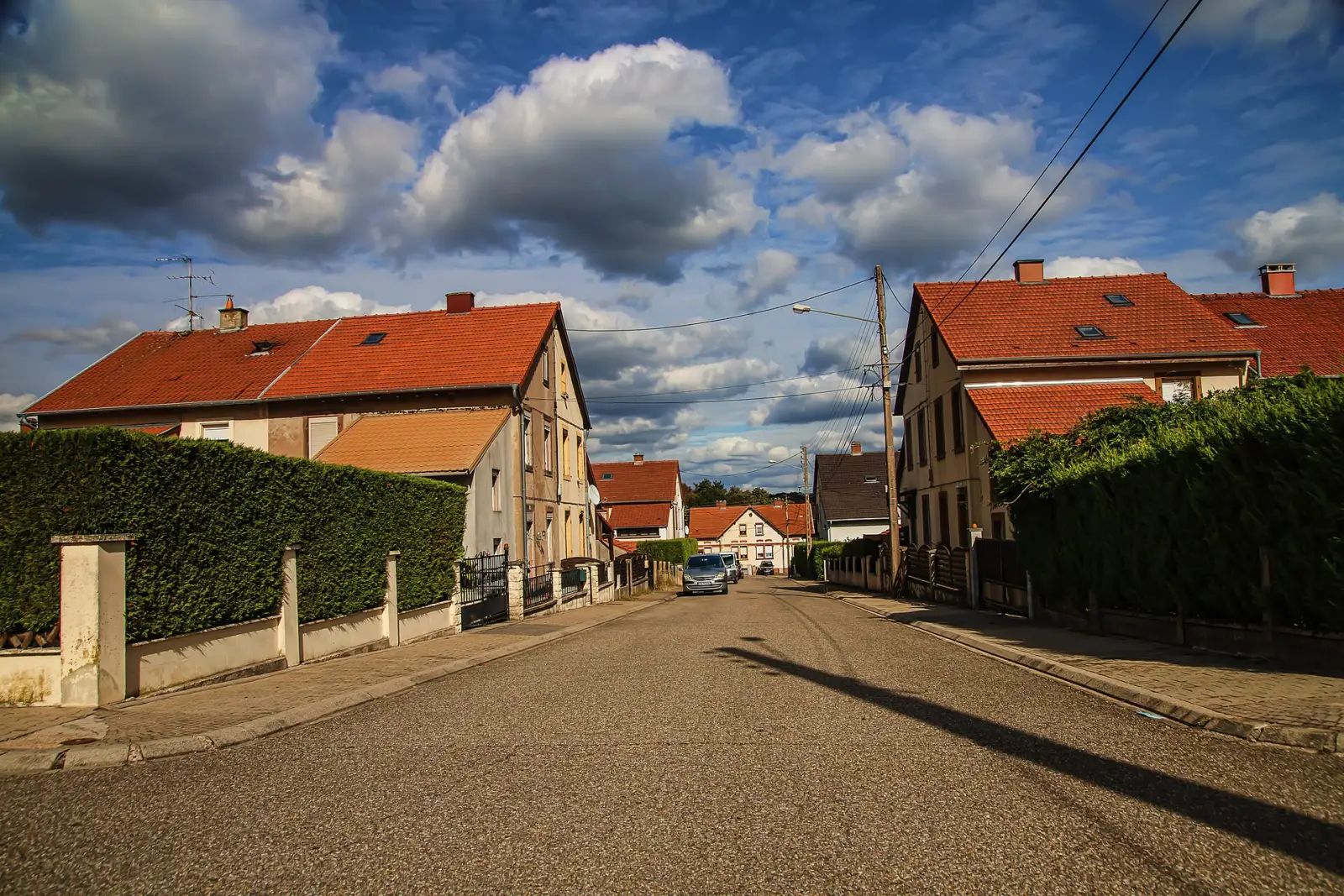 Rue d'une cité minière de Petite-Rosselle bordée de maisons jumelées à toits de tuiles rouges, derrière des haies et des murets