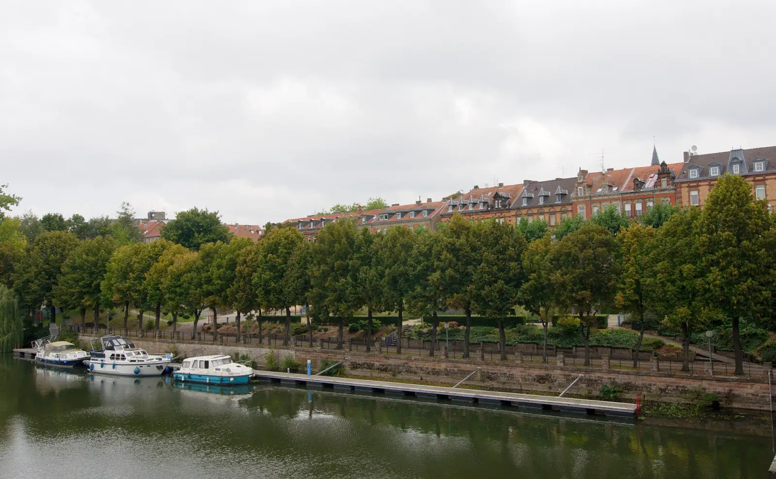 Les quais de la Sarre à Sarreguemines, avec des bateaux de plaisance amarrés, une promenade arborée et une rangée d'immeubles anciens
