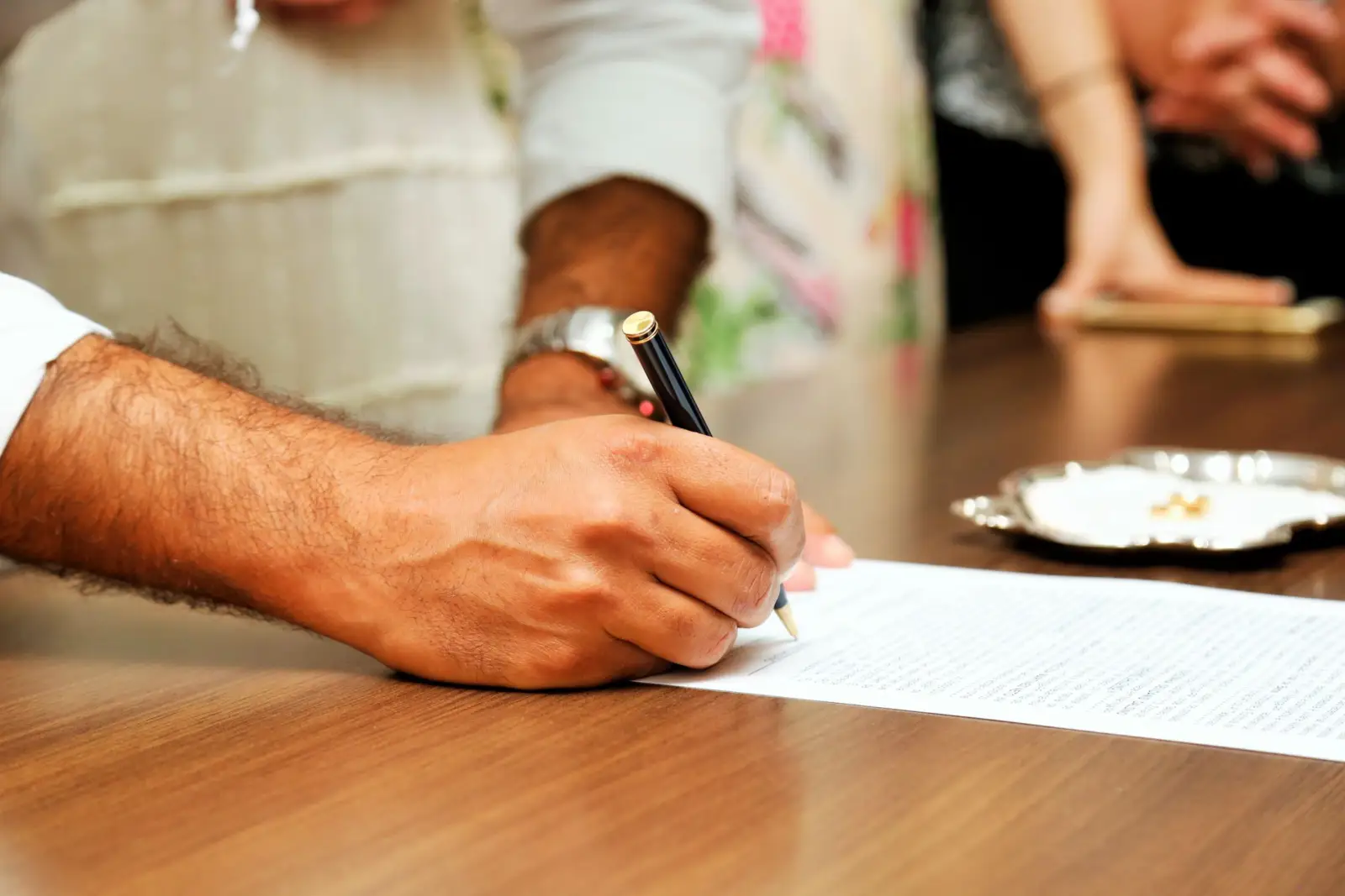 Main d'un homme signant un document au stylo sur une table en bois