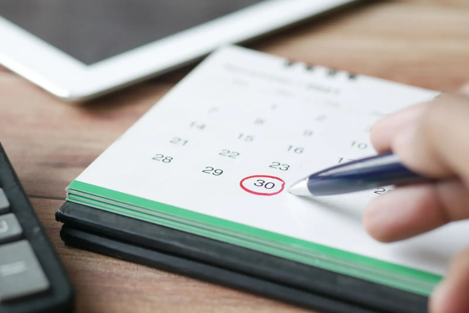 Main tenant un stylo qui entoure une date sur un calendrier de bureau