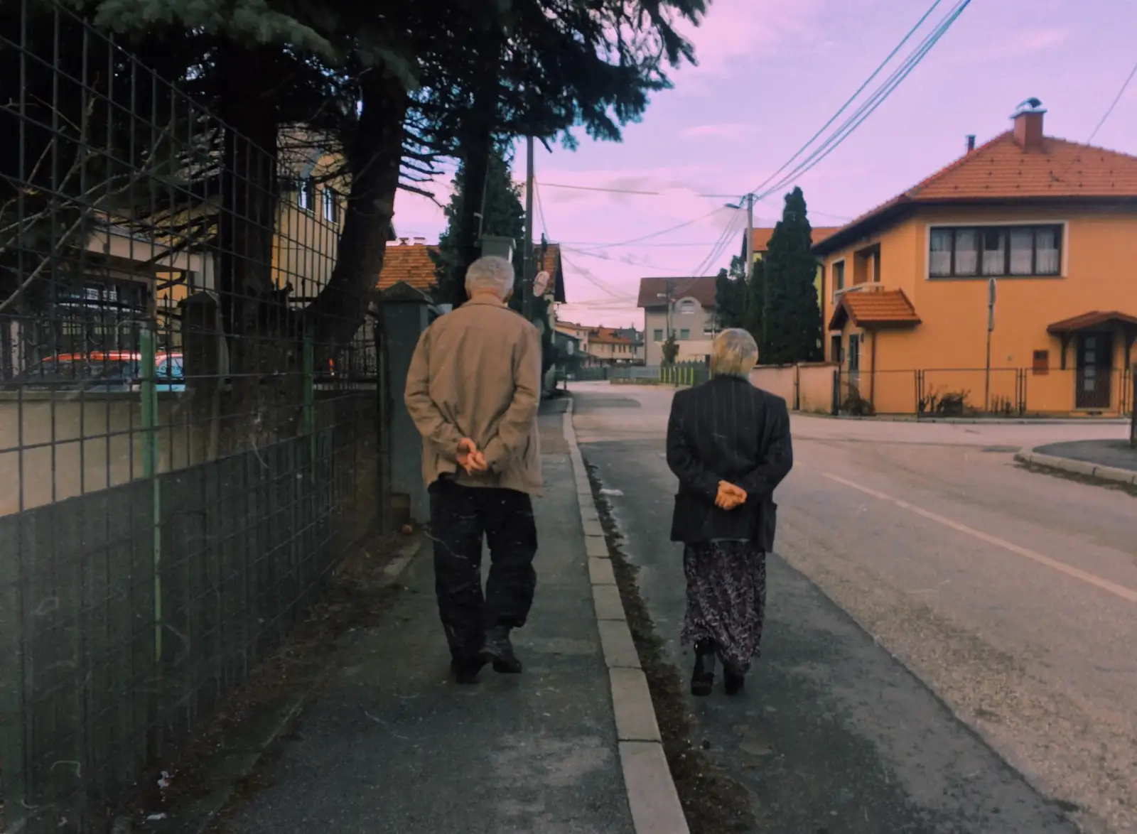 Couple âgé marchant de dos sur le trottoir d'une rue résidentielle bordée de maisons