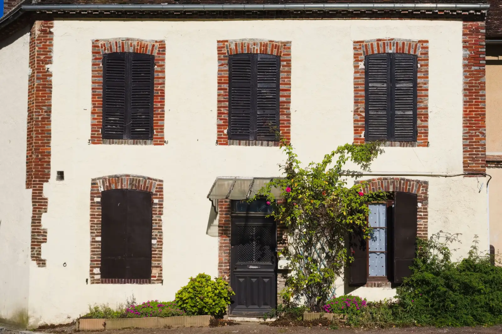 Façade crépie d'une maison ancienne aux encadrements de briques et aux volets de bois, en Île-de-France