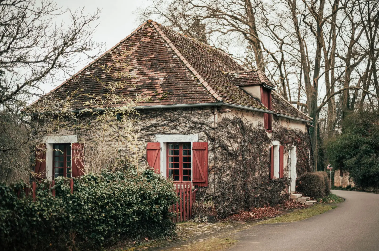 Maison ancienne en pierre aux volets rouges et aux murs couverts de lierre, dans la campagne française