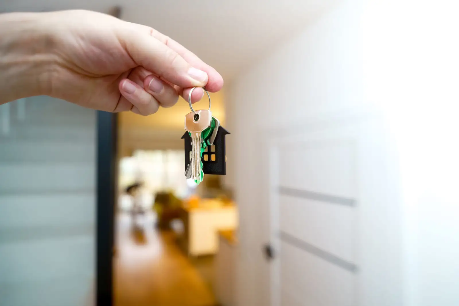 Main tenant un trousseau de clés avec un porte-clés en forme de maison, dans un appartement lumineux