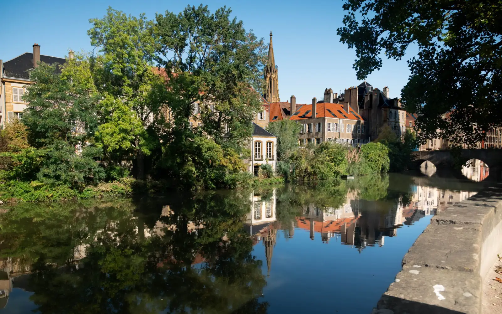 Maisons anciennes aux toits rouges et clocher au bord de l'eau à Metz, sous un ciel bleu