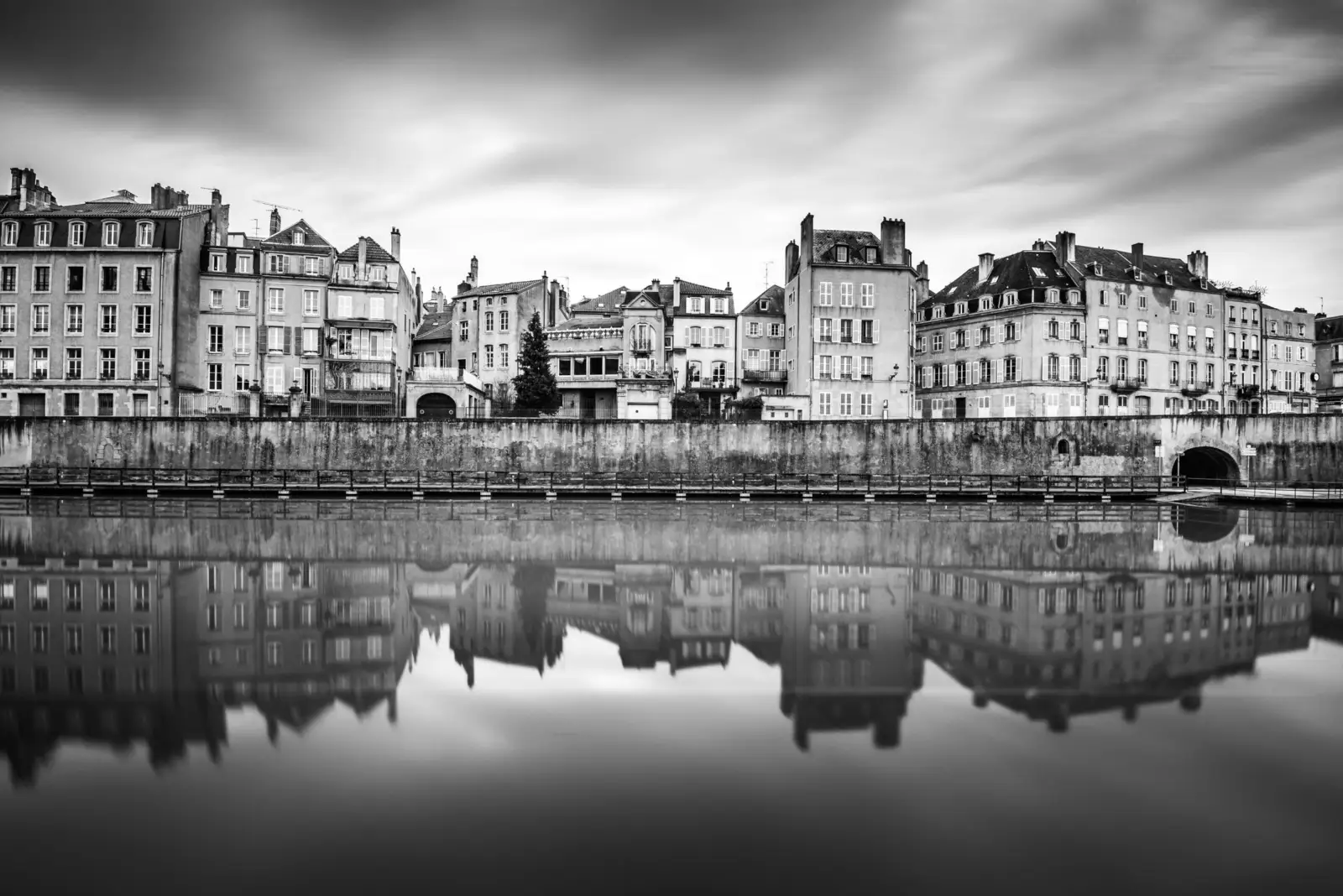 Façades d'immeubles anciens alignés le long d'un quai et reflétés dans l'eau calme, à Metz, en noir et blanc