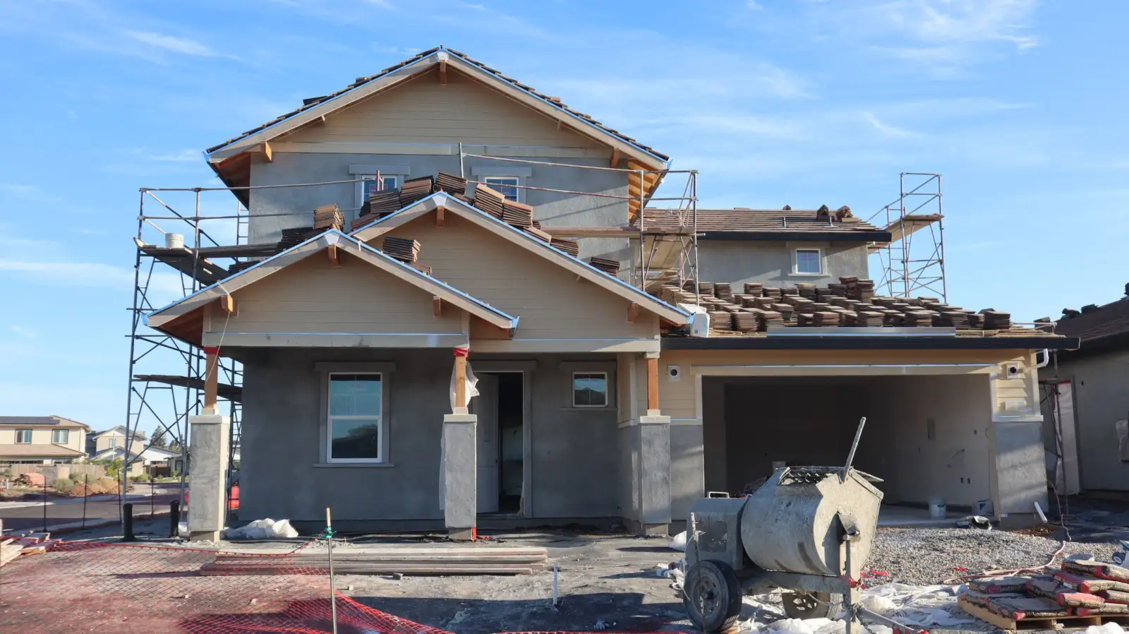 Maison individuelle neuve à étage en cours de construction, avec échafaudages et bétonnière devant la façade