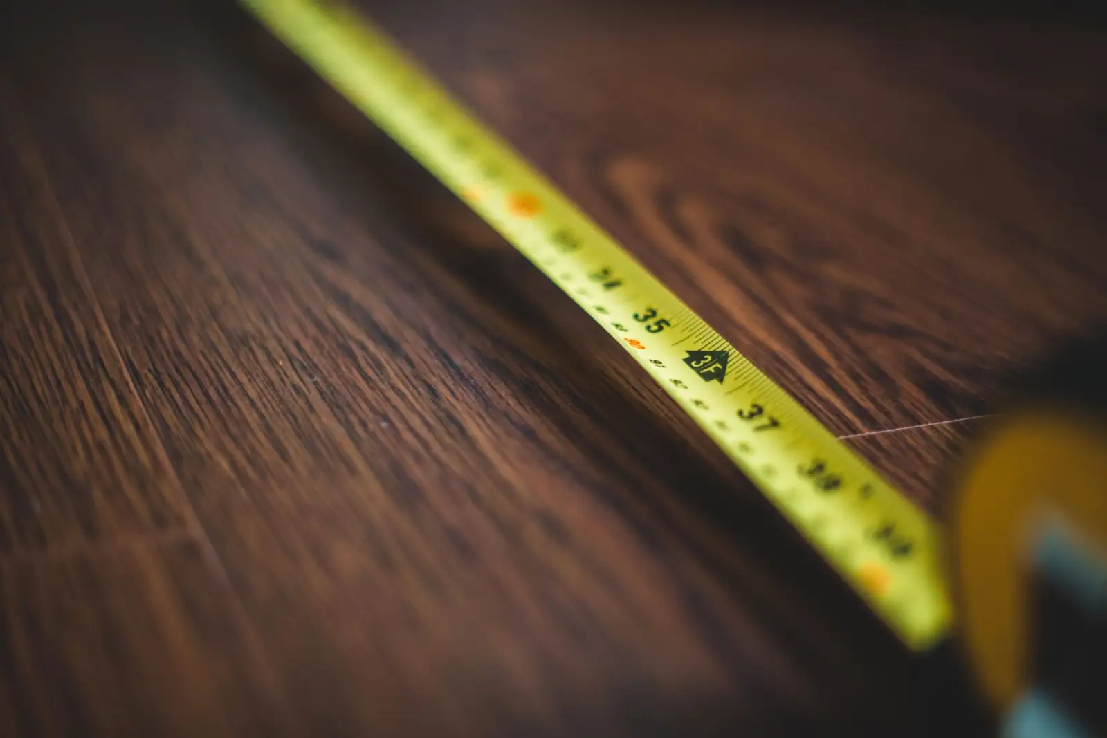 Mètre ruban jaune déroulé sur un parquet en bois sombre