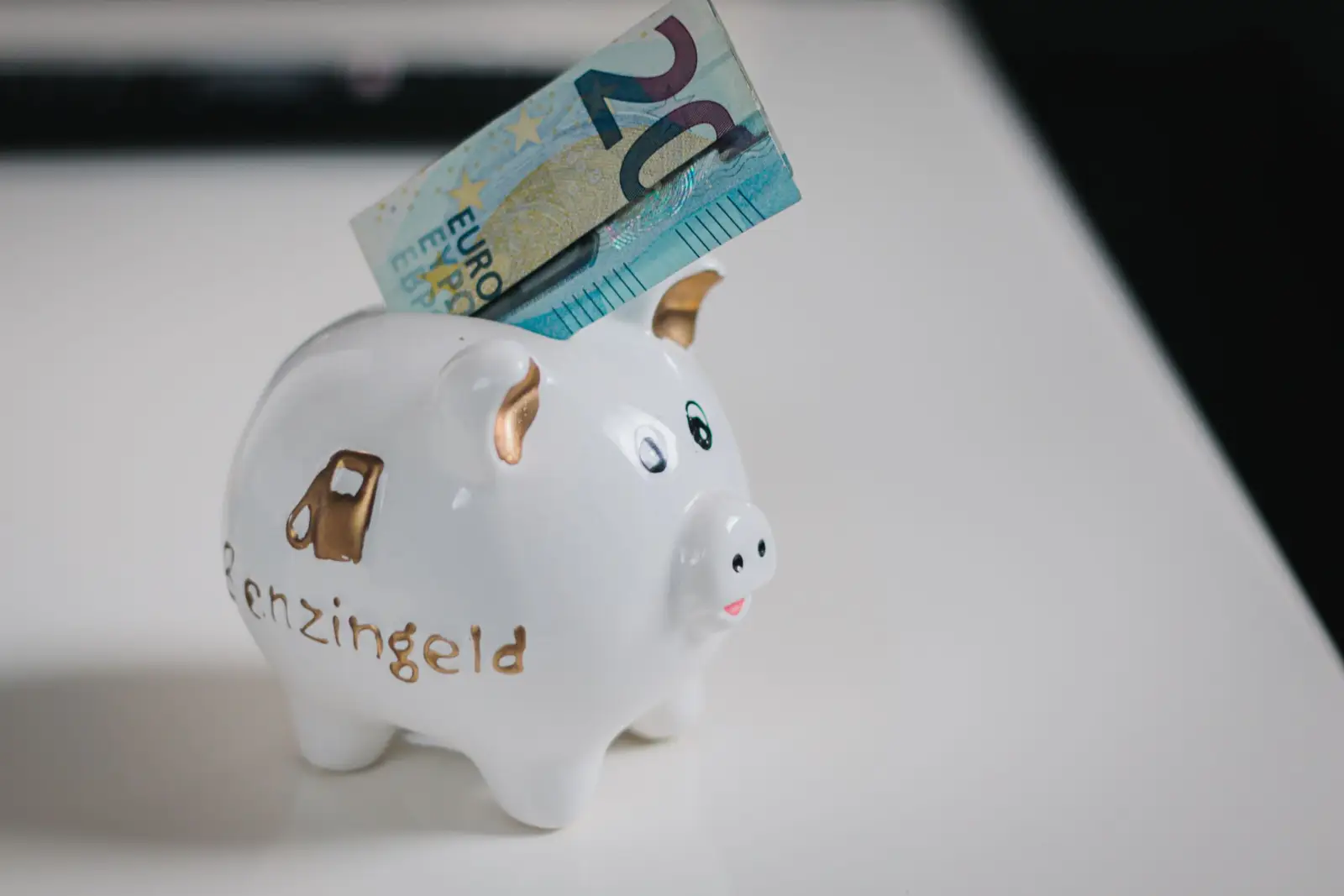 Tirelire blanche en céramique avec un billet de 20 euros glissé dans la fente