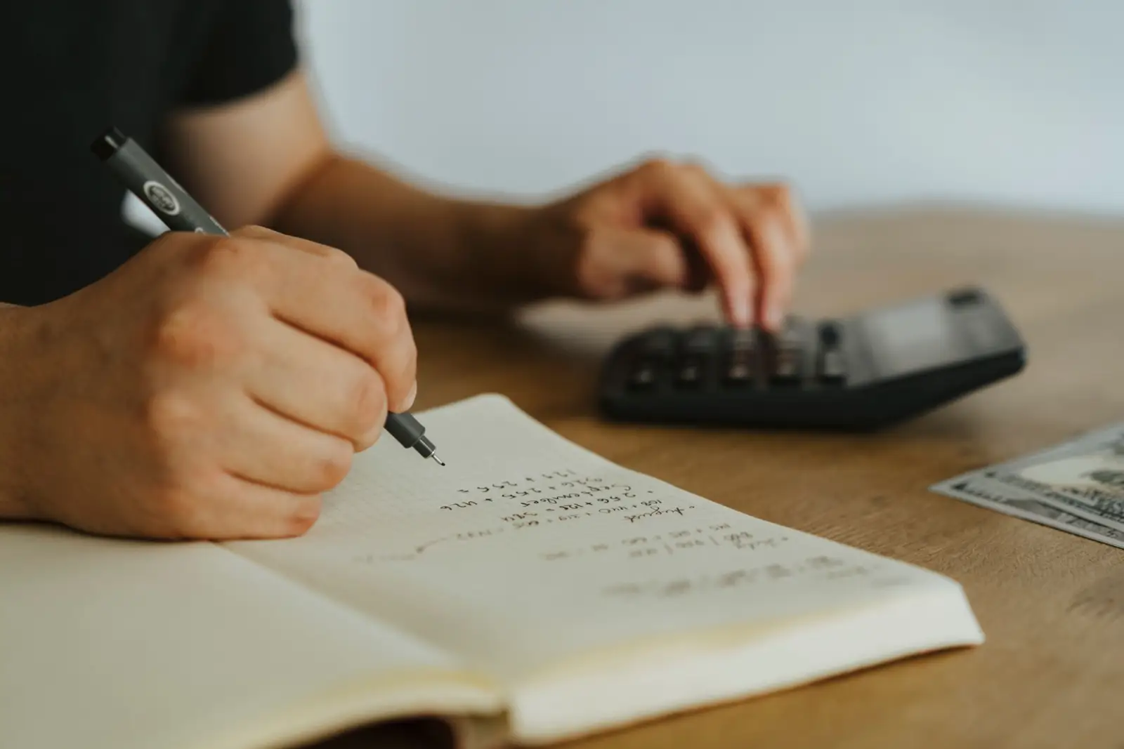 Mains écrivant des calculs dans un carnet à côté d'une calculatrice