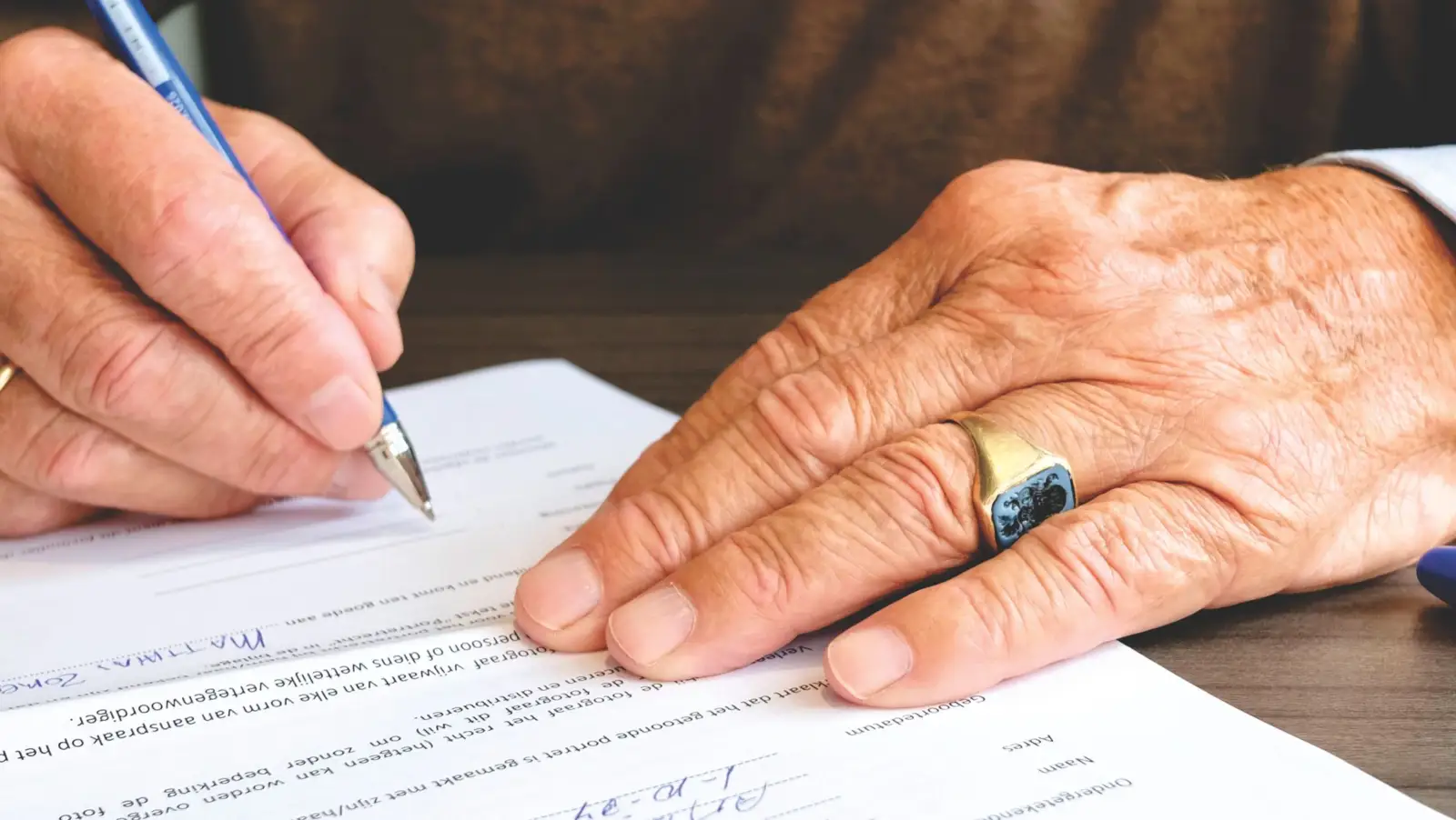 Mains d'une personne âgée signant un document posé sur une table