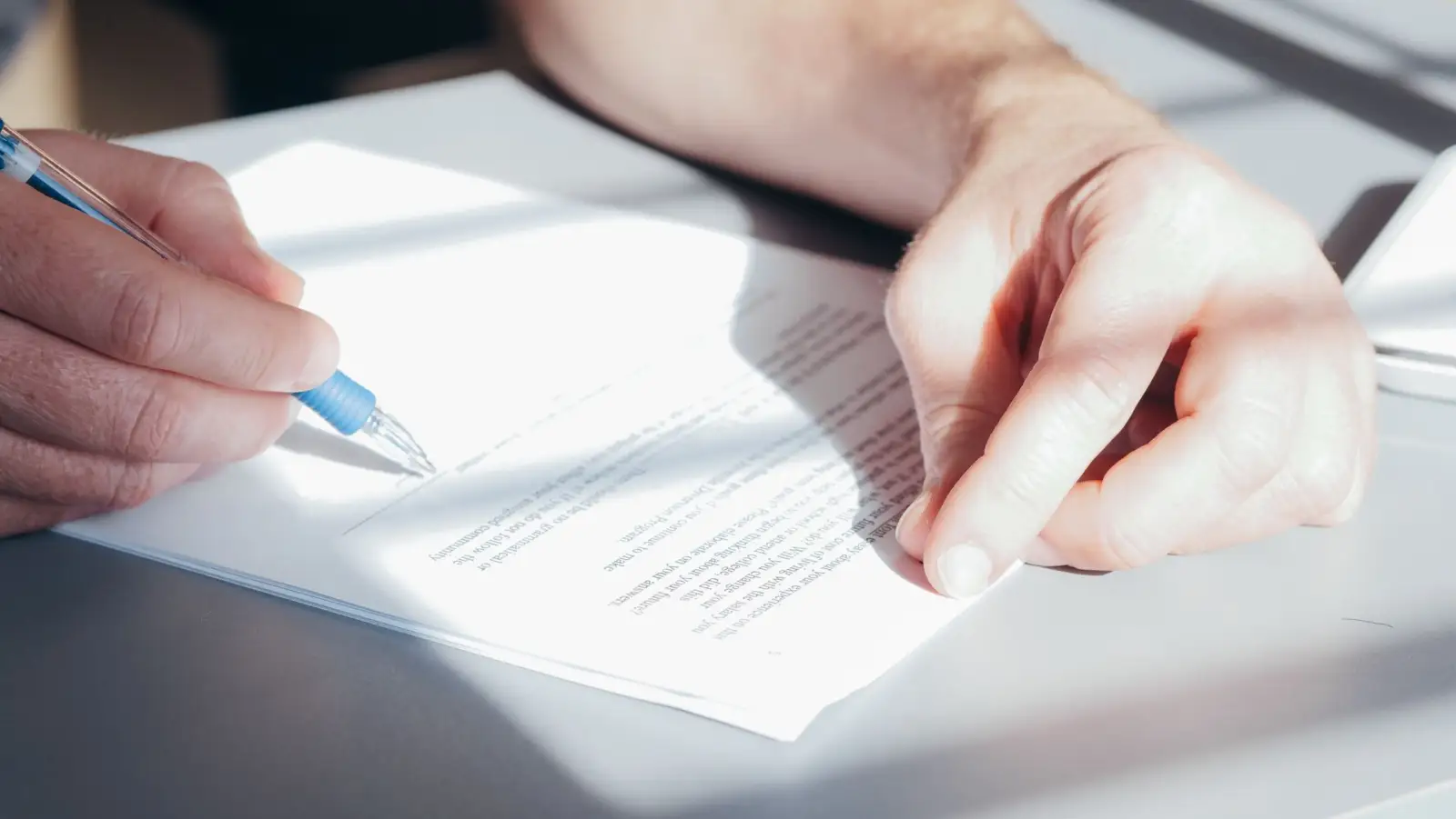Mains qui signent au stylo bleu un document posé sur une table