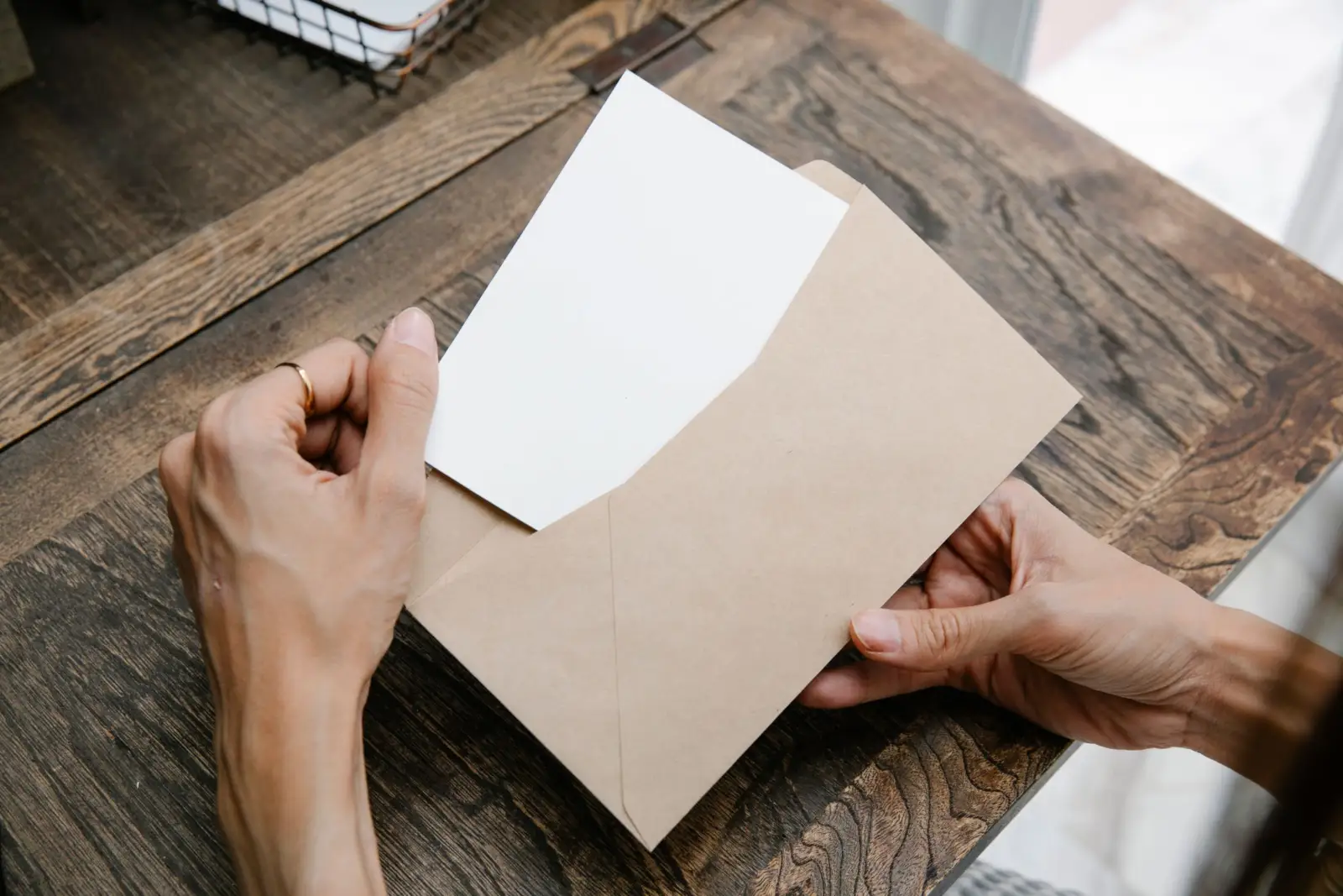 Mains tenant une lettre glissée dans une enveloppe kraft sur un bureau en bois