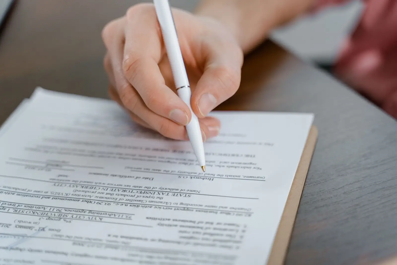 Main tenant un stylo qui signe un document posé sur une table