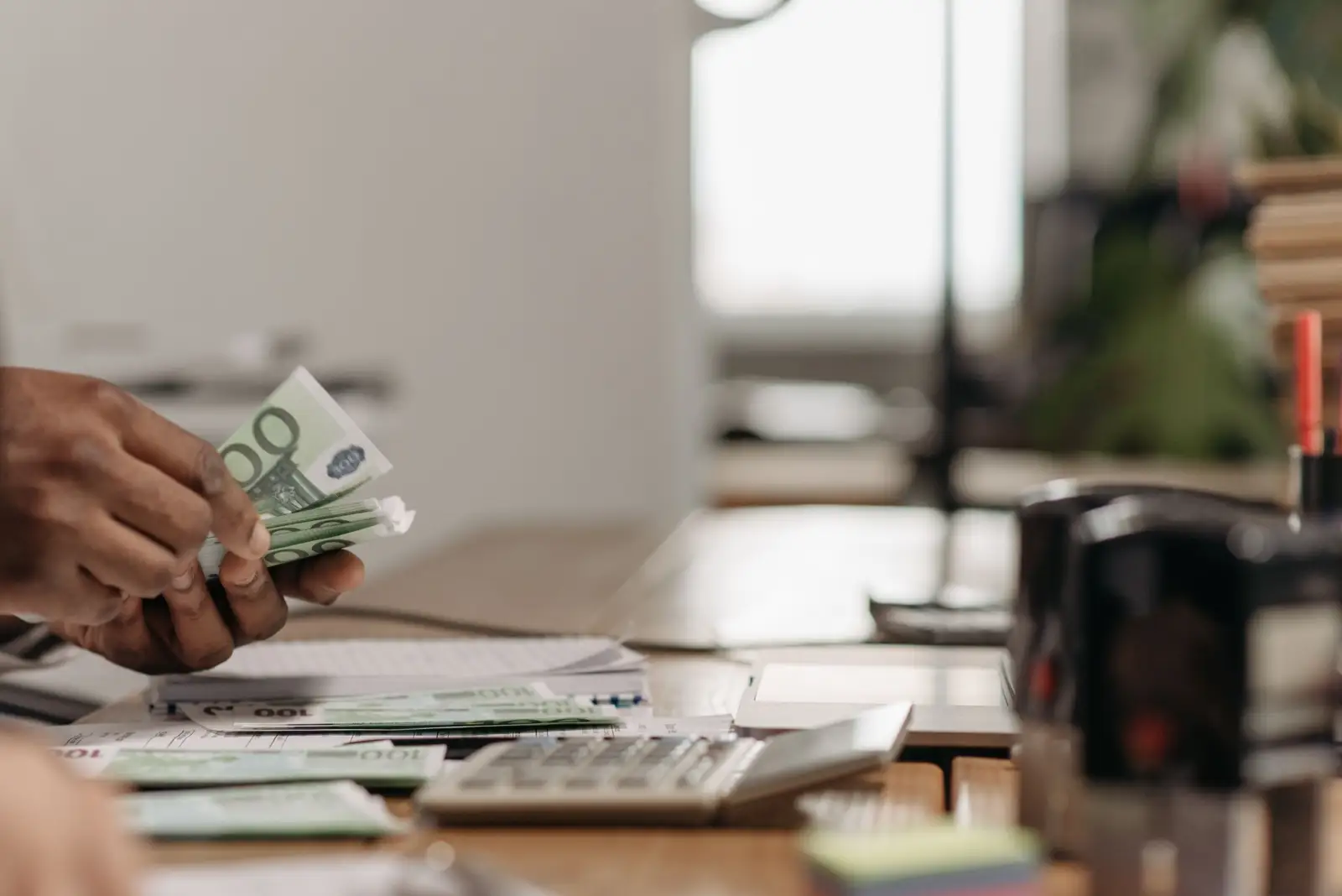 Mains comptant des billets de 100 euros au-dessus d'un bureau avec une calculatrice et des documents