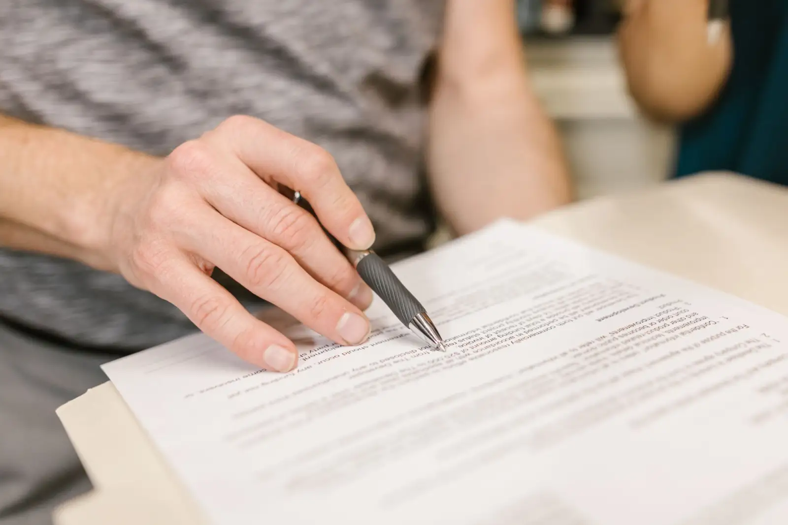 Main tenant un stylo au-dessus d'un contrat imprimé posé sur une table