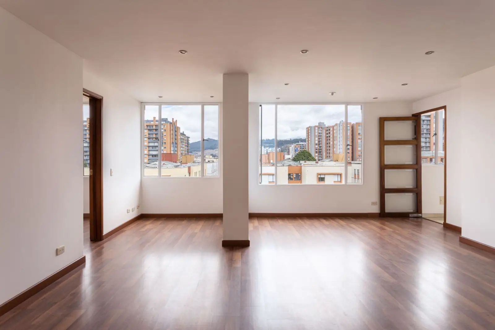 Pièce vide et lumineuse d'un appartement, avec un parquet en bois et de larges fenêtres